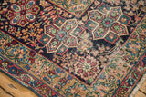 Antique Persian Kerman carpet detail: pinwheel floral pattern, cochineal red, sky blue, and visible pile wear.