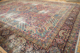 Detail of antique Kerman carpet showing intricate floral border, rich colors, and visible wear.