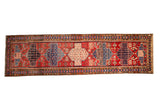 Vintage Persian Baktiari runner with repeating geometric medallions in blue, navy, and blush over a brick red field.