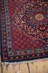 Corner detail of a vintage Persian Kashan rug, showing the intricate borders and worn, frayed fringe.