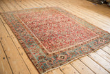 Angled perspective of an antique Heriz rug showing its cherry red Herati field and dusty teal border.