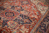 Detailed angled view of the geometric arabesques in cherry red and navy blue on a vintage Heriz rug.