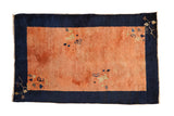 Antique Peking rug with a dusty rose terracotta field, a wide navy blue border, and delicate floral vines.