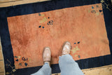 Person's view of the antique Peking rug's low pile and dusty rose terracotta field.