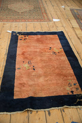 Angled view of an antique Peking rug highlighting its copper-rose field and wide navy border.