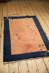 Antique Peking rug from an angle, featuring a spacious terracotta field against a deep navy blue border.