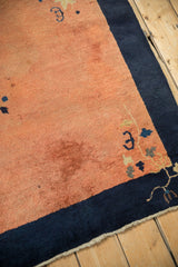 Antique Peking rug corner showing time-softened dusty copper pile and a navy blue border.