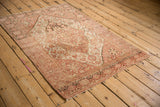 Angled perspective on a distressed Farahan Sarouk rug, with abrashes across its dusty rose field.