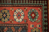 Starburst medallions and pawn motif border in jade, blue, and ochre on a red antique Kazak rug.