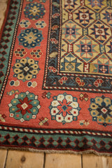 The intricate blush floral border and outer pawn motif of an antique Kazak rug corner.