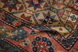 Dense, hand-knotted texture of a folded antique Kazak rug with saffron, blush, and cobalt geometric motifs.
