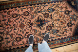 Overhead view of the elaborate navy vine pattern on a dusty magenta and camel vintage Persian rug.