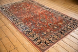 Angled view of a vintage Sarouk carpet with a brick-red field and dense floral sprays.