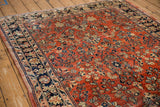 Angled view of a vintage Sarouk carpet's intricate navy border next to its brick-red floral field.
