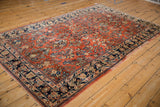 Vintage Persian Sarouk carpet with dense floral sprays on a brick red field, shown at a high angle.