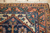 Vintage Heriz rug corner detail with cream fringe, dusty rose serrated border, and blue blossom motifs.