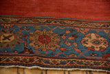 Deep sapphire blue border of an antique Persian Sultanabad rug with colorful palmettes and red field, showing fringe.