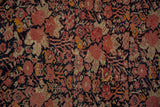 Antique Malayer rug close-up: dusty blush floral motifs, navy outlines, tangerine accents, subtle wear.