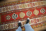 A view looking down at the antique Kazak runner's textured pile, geometric guls, and wide ivory borders.