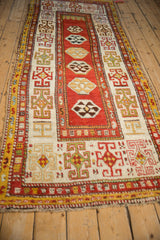 Antique Caucasian Kazak runner from an angle, showing its linear medallion pattern and elaborate geometric borders.