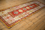 Antique Kazak rug runner viewed from an angle, showing the full length and geometric medallion design.