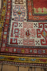 Textured view of an antique Kazak rug's geometric serpent and ram's horn border motifs.