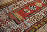 Hand-knotted texture of a Kazak rug's geometric rams horn border in red, blue, and ivory.