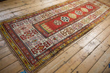 Diagonal view of an antique Caucasian Kazak runner with a madder red field and geometric gul borders.