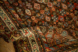 Folded antique Kurdish Hamadan runner, revealing textured pile and intricate floral patterns in madder red, ivory, and mallard green.