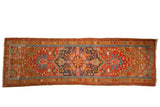 Antique Heriz rug runner with a large navy blue geometric medallion on a soft cherry red field, framed by a gold ochre border.