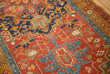 Detail of an antique Heriz rug showing geometric motifs on a cherry red field next to a gold ochre border.