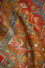A soft fold in an antique Heriz runner shows the textured pile and palette of gold ochre, blue, and jade green.