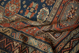 Textured weave of a folded antique Soumac carpet, showing zig-zag borders and gul motifs in madder red and navy blue.