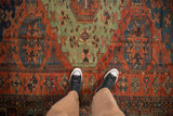 A top-down view showing the scale of the antique Soumac carpet's geometric field in madder red and jade green.