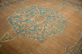 Angled view of the scalloped medallion in dusty blue on the antique Kerman's abrashed sand field.