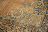Scrolled arabesque corner spandrel in dusty blue and navy on a sand-colored antique Kerman rug.