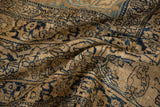 Texture of a draped antique Kerman rug revealing worn navy blue vines on a tea-washed sand and beige ground.