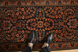 Vintage Sarouk runner with navy ground, dense coral floral sprays, and palmette vine border.