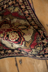 Angled close-up of the antique Yezd mat's low pile and cochineal red floral motifs.