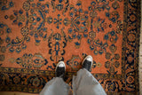 Feet on antique Persian Lilihan rug with dusty rose floral sprays and blue Herati motif.