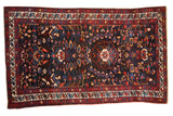 Vintage Bakhtiari rug with a staggered center medallion and tree of life motifs in gem tones on a navy blue field.