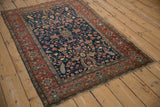 Antique Farahan Sarouk rug from an angle, detailing its navy field, central medallion, and red border.
