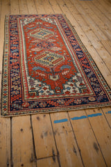 Vintage Heriz rug runner corner with short ivory fringe and geometric brick red and blue border.