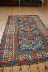 Antique Kazak rug border with repeating floral blossom motif in madder root red, blue, and beige tones.