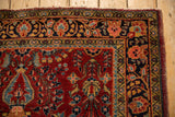 Corner detail of a vintage Persian Sarouk showing floral borders in navy blue and sand beside the cherry red field.