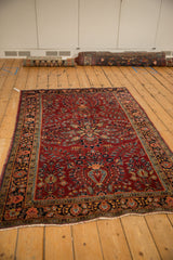 Vintage Sarouk rug with a starburst medallion and cherry red floral field, shown from an angle.