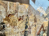 Angled detail of mixed media art with textured gold leaf, script, and layered paper.