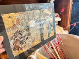 Lillian Shad's framed mixed media collage shown at an angle, highlighting its gold leaf detail.