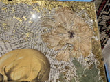 Mixed media art corner showing gold leaf texture, a dried flower, and an anatomical skull over text.
