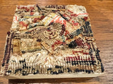 Angled view of the layered antique rug fragments creating a dimensional, textured surface.